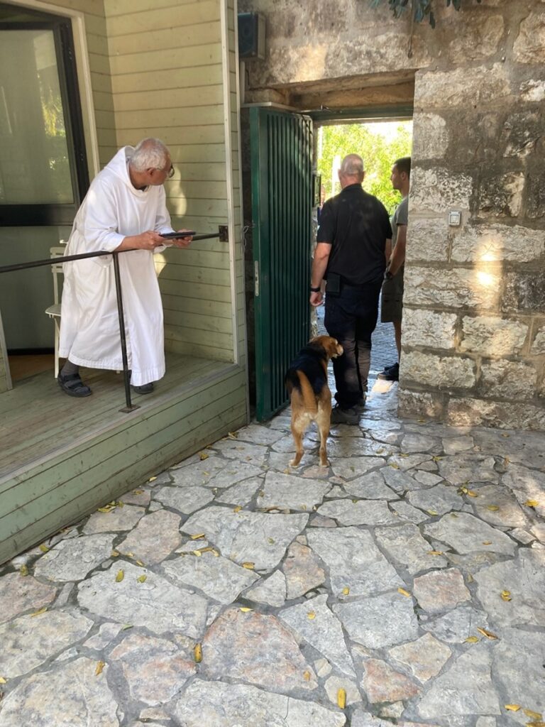 Mönch bei Klosterpforte mit Tablet und Männer mit Hund im Gespräch