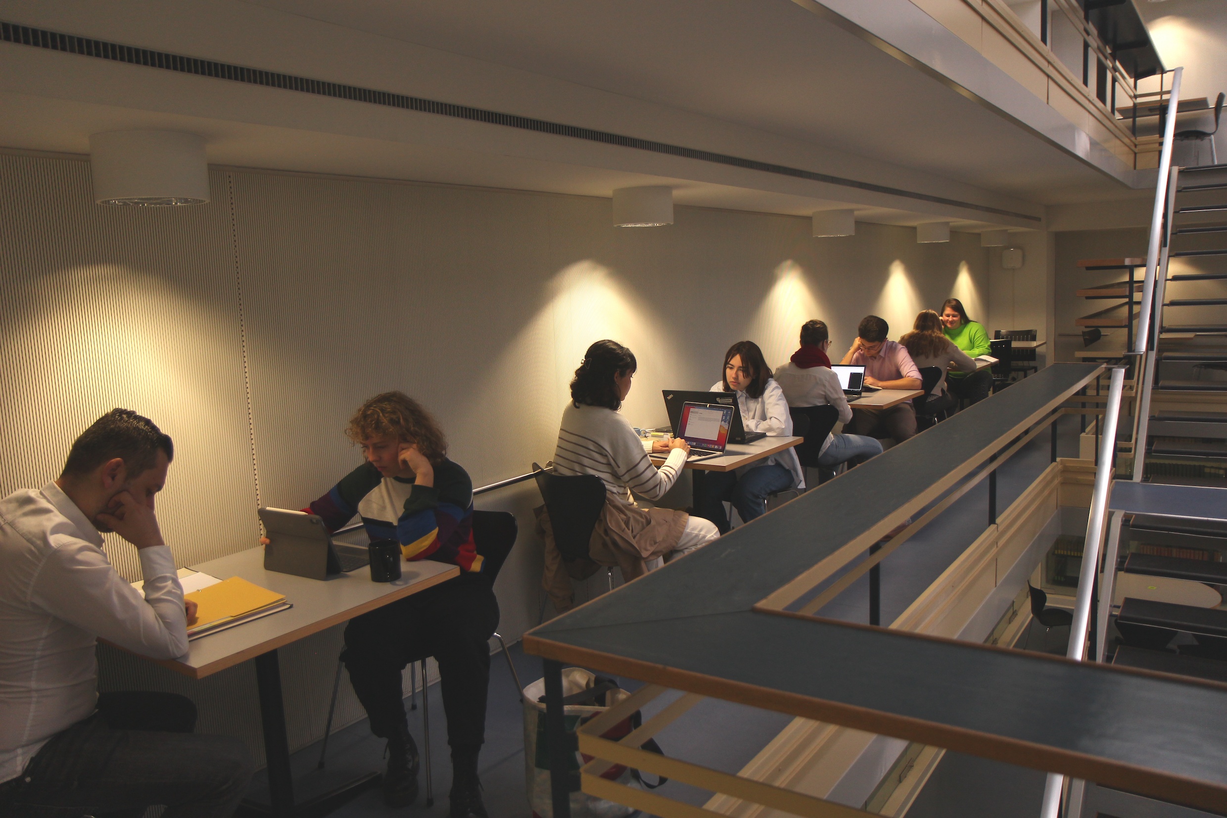 Das Bild zeigt Studierende, die an kleinen Tischen im Lernraum am DS sitzen und konzentriert arbeiten. Es ist eher dunkel, die Arbeitsplätze sind mit hellen Lichtkegeln beleuchtet.