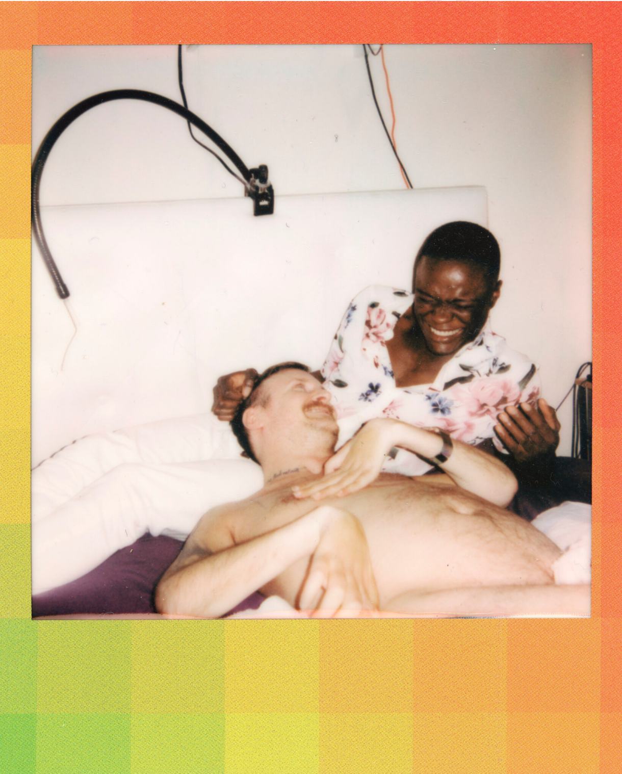 untitled, 2021.  [Image description: A polaroid photograph of two men lying on a bed and laughing. One of them, a white naked man, is the artist Robert Andy Coombs. His head is resting on the lap of his friend Marshall, a Black man wearing a shirt with flowers and white trousers, Behind them, a sip-and-puff-device and cables are attached to the headrest. The frame of the polaroid is colored in grades of green to orange.] 