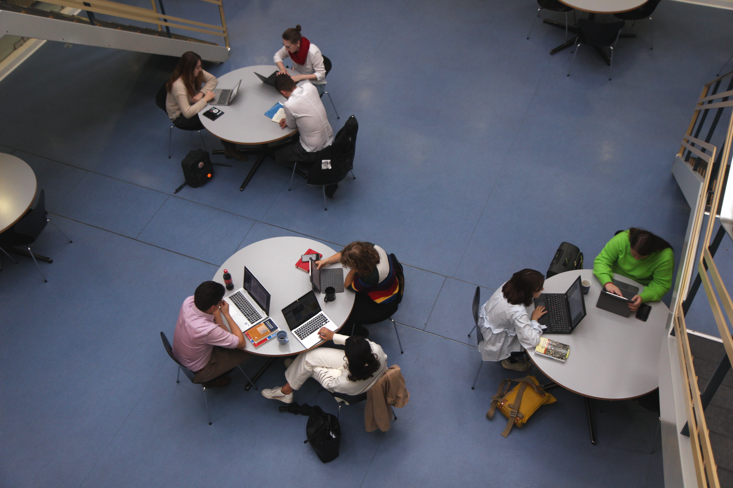 Das Bild zeigt drei runde Tische im Lernraum am Deutschen Seminar, an denen Studierende arbeiten.